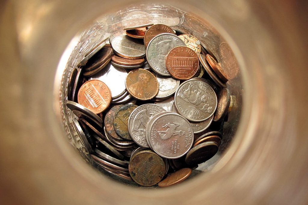 Looking down into a glass jar of mixed US coins: pennies, nickels and state quarters.