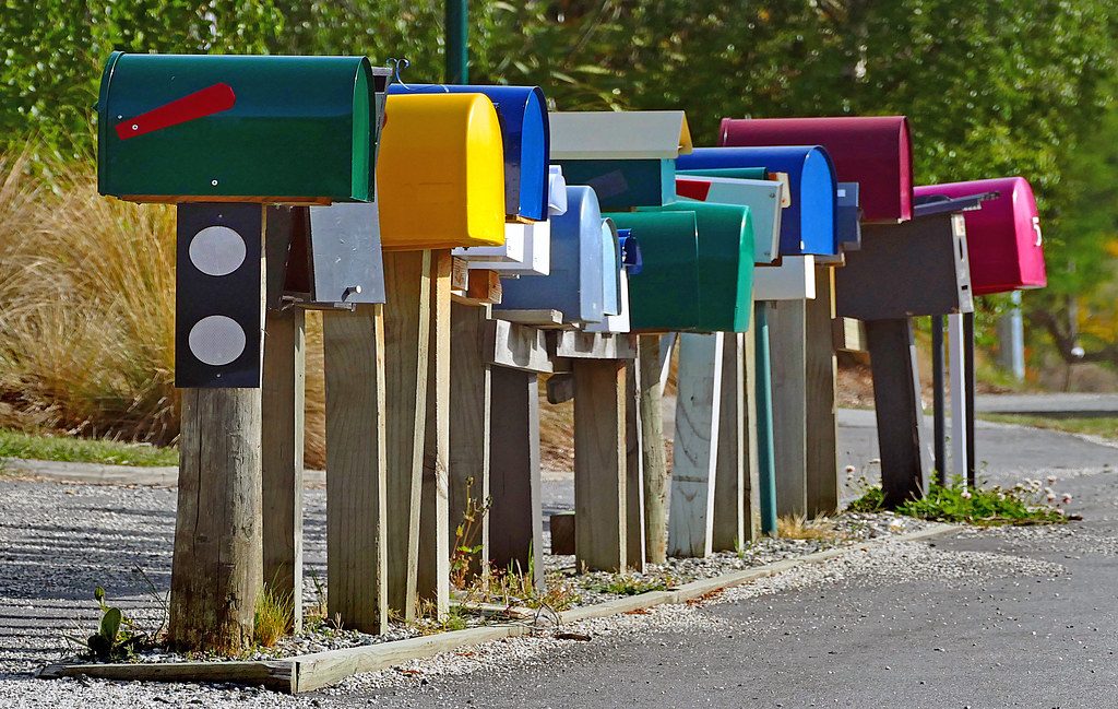 A row of colourful rural mailboxes on wooden posts beside a quiet road.
