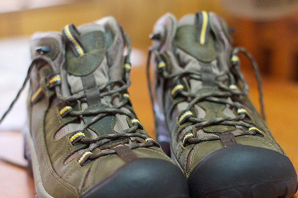 A pair of olive-green leather and mesh hiking boots with yellow-trimmed laces, close up on a wooden surface.