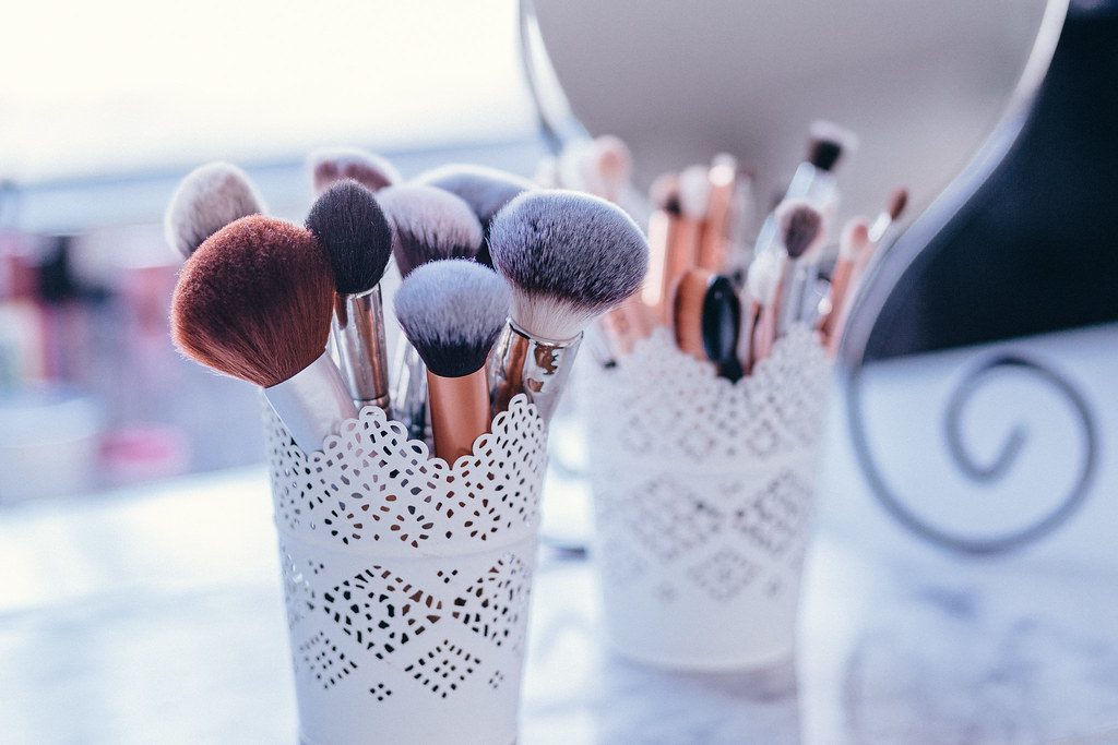 Makeup brushes standing in white lace-pattern holders on a dressing table beside a mirror.
