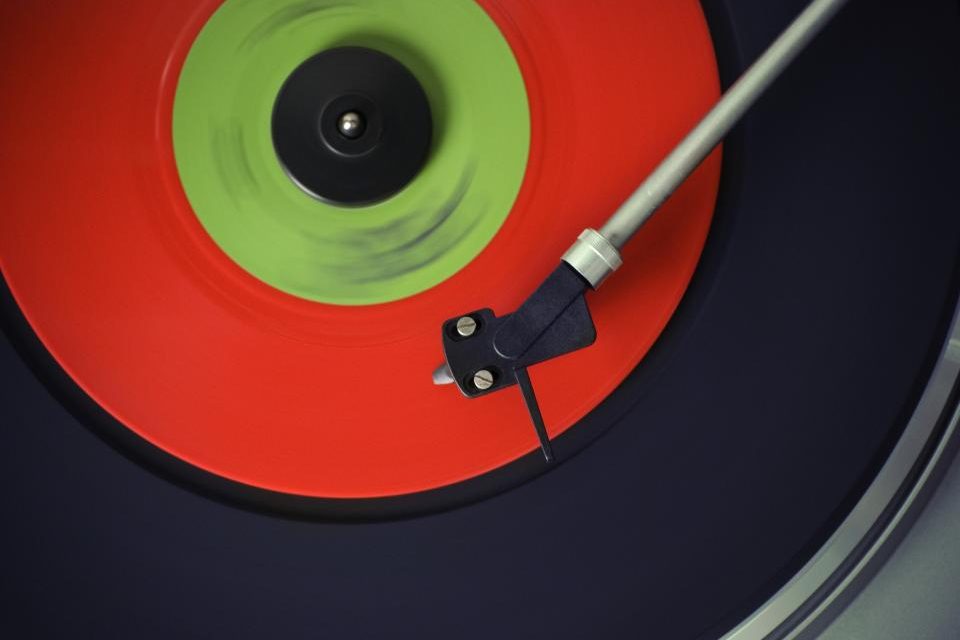 A bright red and green vinyl record spinning on a turntable with the tonearm and stylus on the groove.